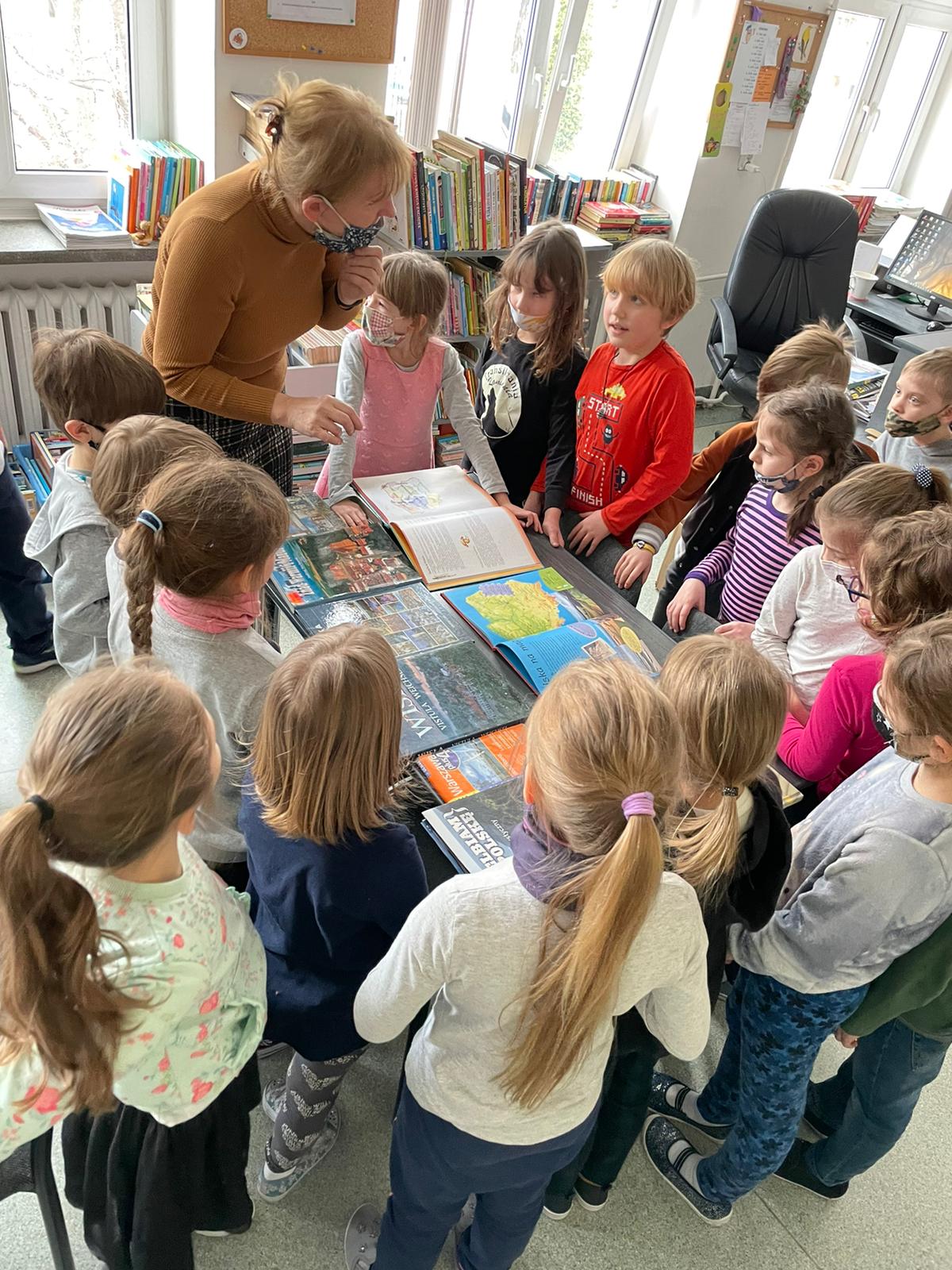 Dzieci z klasy 1a oglądają w bibliotece książki o Polsce, które pokazuje Pani bibliotekarka.