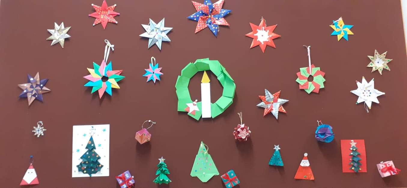 Zdjęcie przedstawia brązową tablicę, na której umieszone ozdoby świąteczne (gwiazdki, choinki, bombki) wykonane techniką origami.