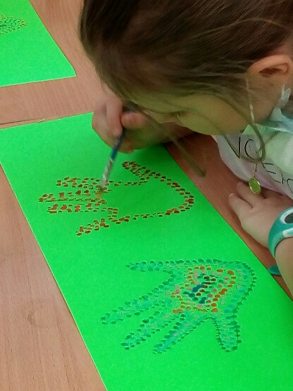 Na zielonej kartce dziewczynka maluje łapki metodą kropkowania.