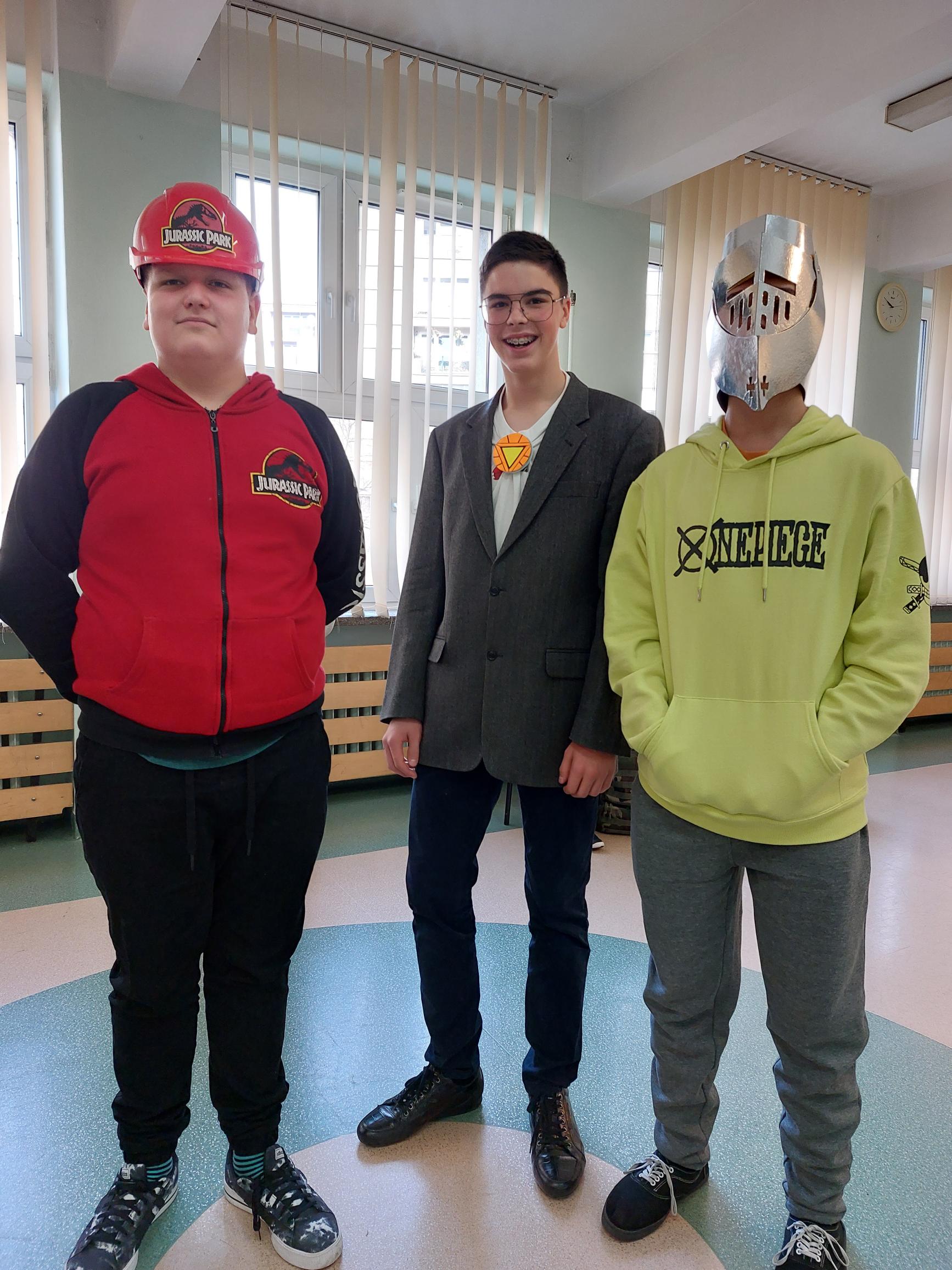 Trzech chłopców stoi w korytarzu, dwóch ma maski na twarzach.
