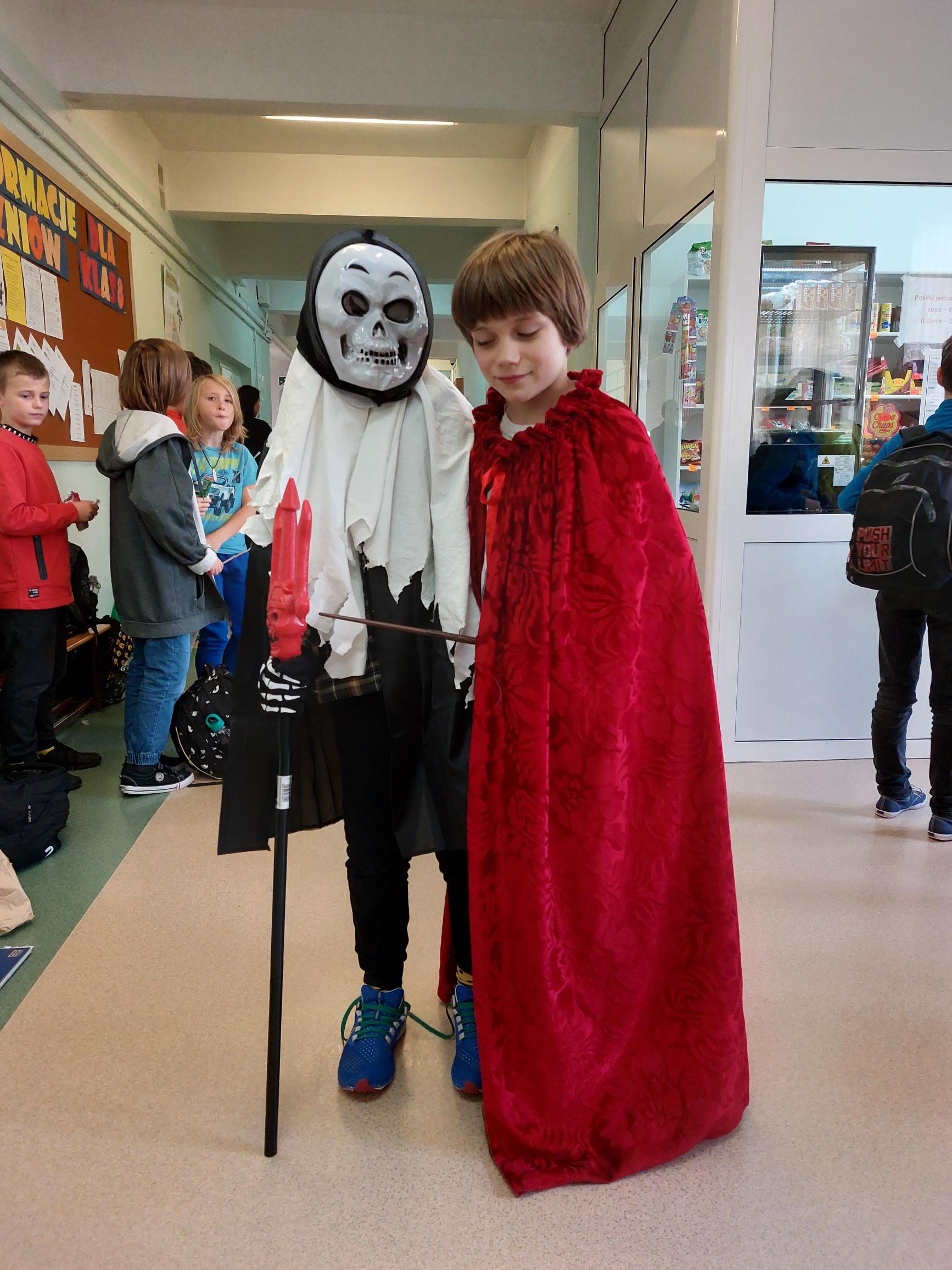 Chłopak w długim, czerwonym płaszczu stoi obok chłopaka w masce.