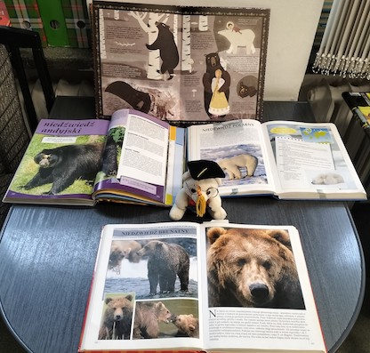 Na stoliku leżą trzy książki otwarte na ilustracjach niedźwiedzi. Wystawa prezentuje plakaty z sylwetkami najbardziej znanych „misiowych” bohaterów literackich.