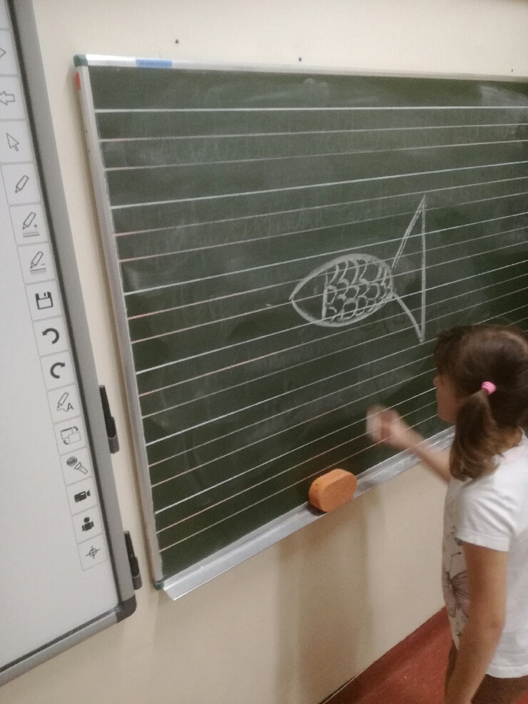 Uczennica rysuje rybę na szkolnej tablicy.