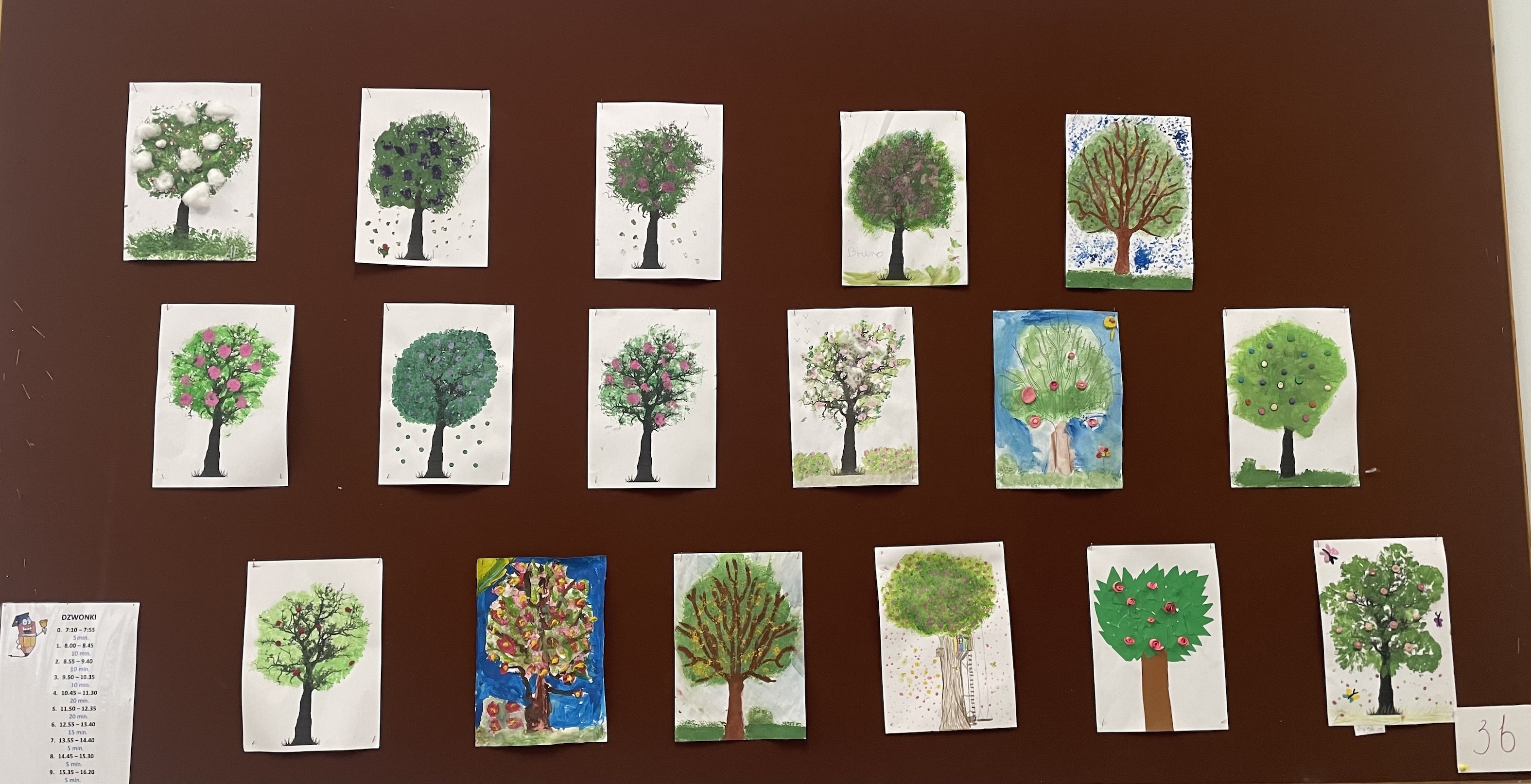 Tablica ścienna przedstawiająca prace uczniów z wiosennymi drzewami.
