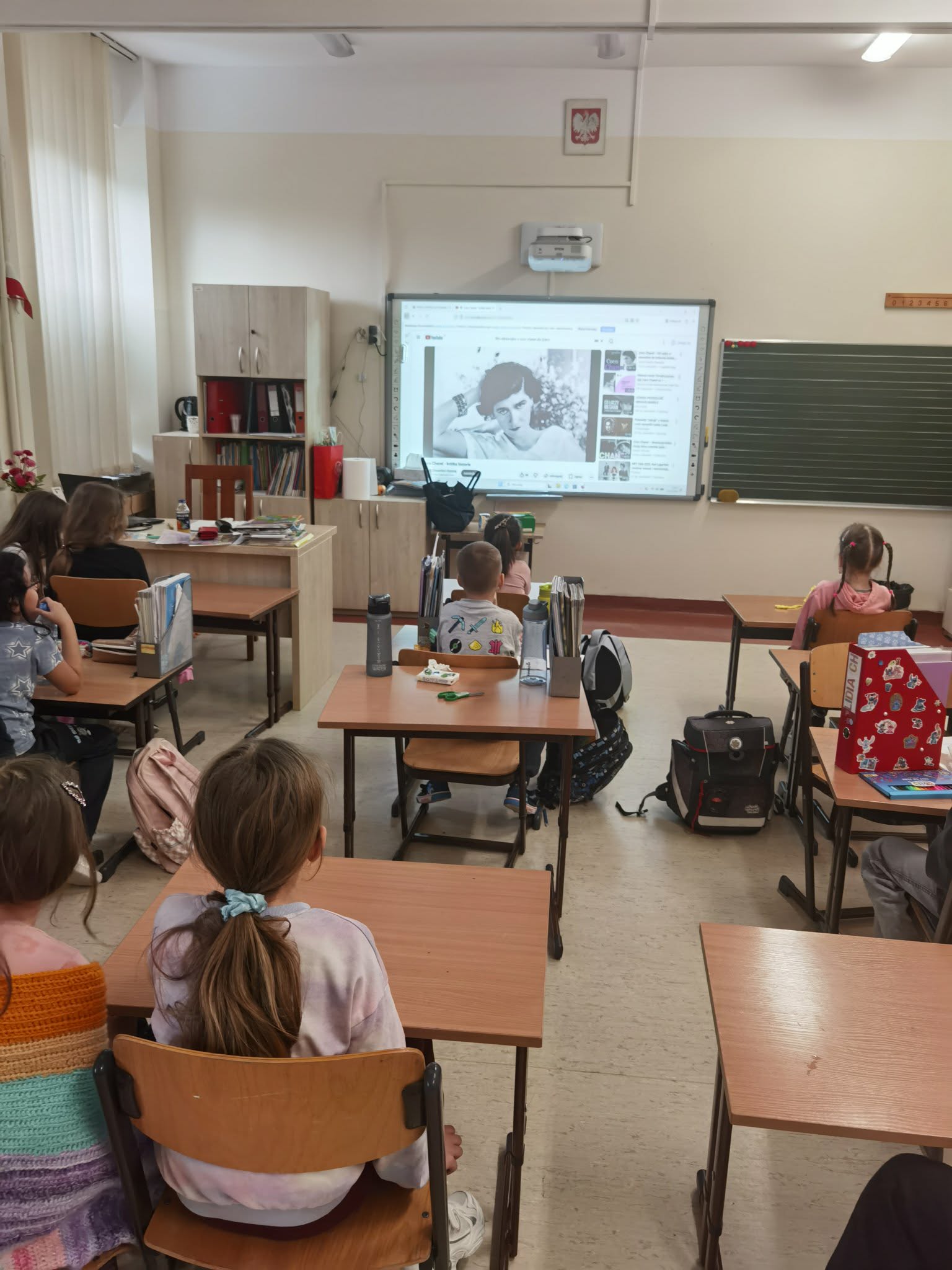 Uczniowie siedzą w ławkach i oglądają fragment filmu.