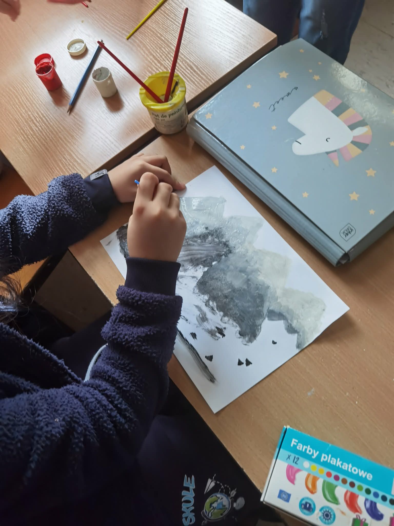 Uczeń maluje farbami.