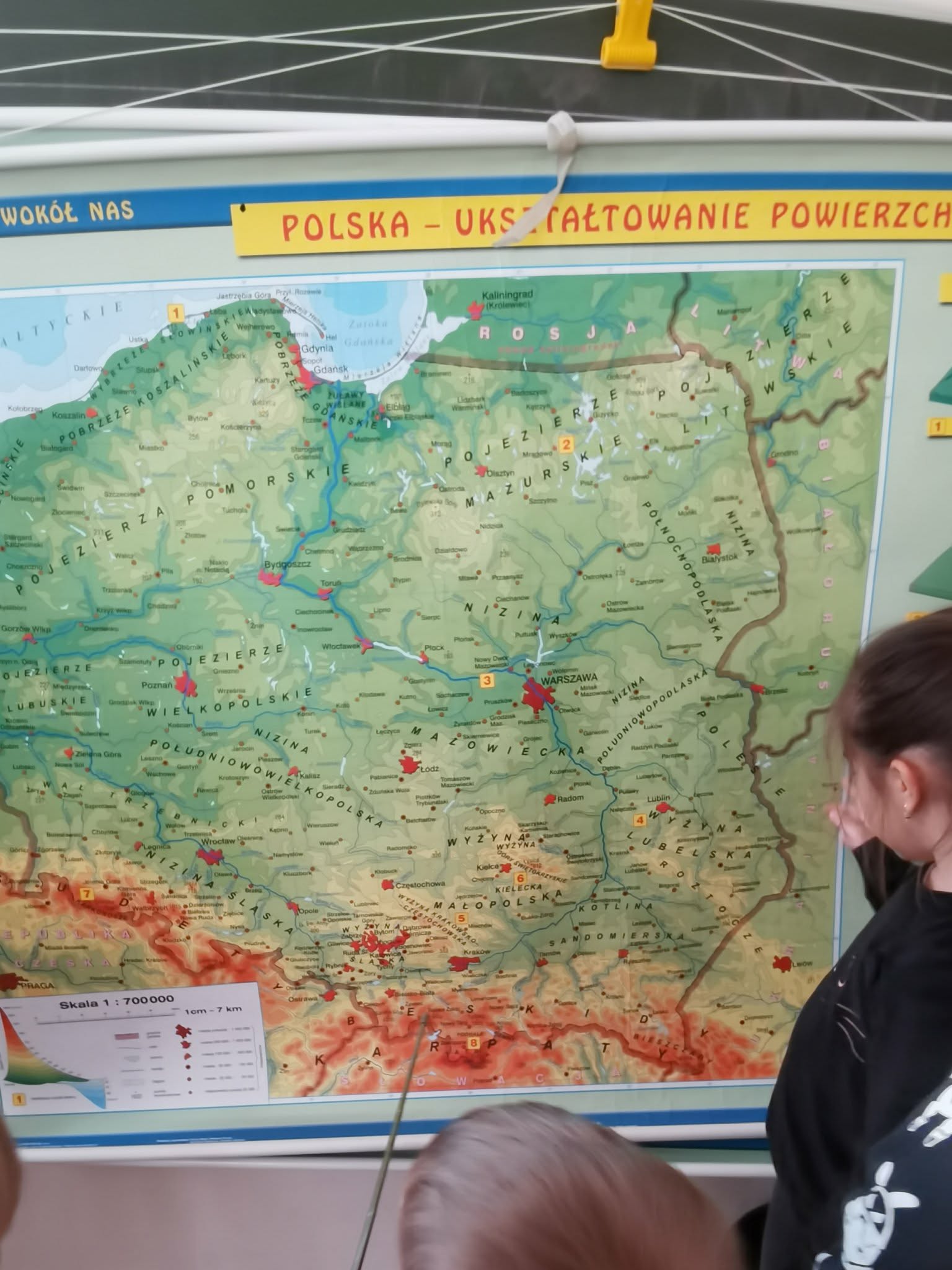 Uczniowie stoją przed mapą Polski.