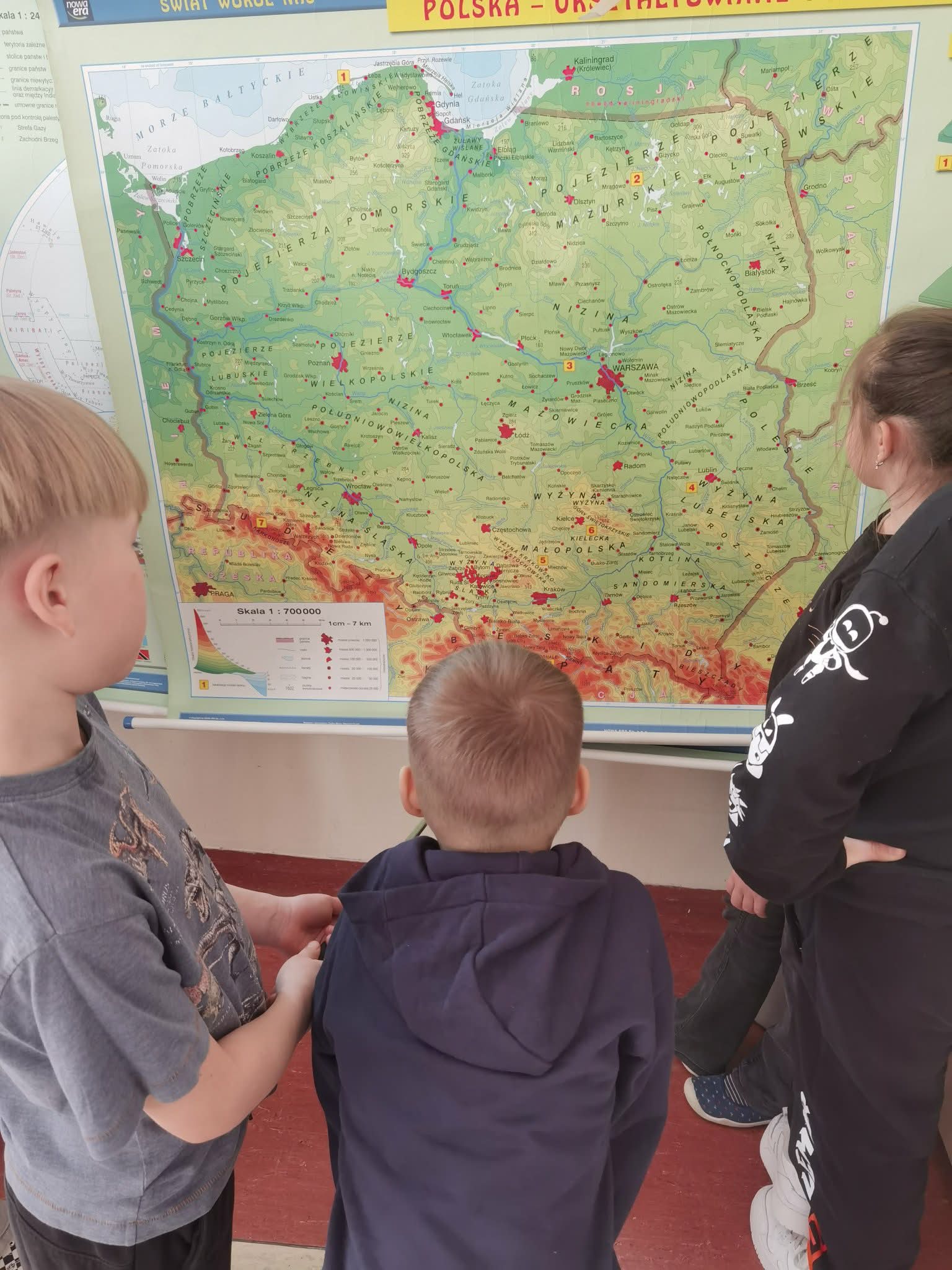 Uczniowie stoją przed mapą Polski.