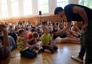 Uczniowie siedzą na podłodze w sali gimnastycznej podczas spotkania w ramach akcji Stop Udarom.