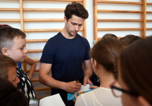 Aktor biorący udział w kampanii rozdaje autografy uczniom.