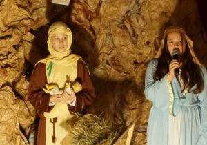 Józef trzyma w swoich ramionach figurkę Dzieciątka Jezus, a Maryja śpiewa kolędę „Lulajże, Jezuniu”.