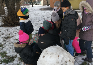 Dziewczynki próbują podnieść kulę śnieżną.