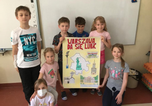 Dziewczynki i chłopcy z klasy 2b prezentują wykonany plakat reklamujący miasto Warszawę.