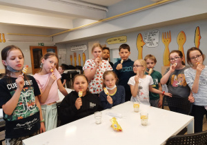 Uczniowie stoją w stołówce i jedzą lody.