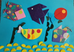 Praca Eleny Latoszek z kl. 1b wykonana techniką origami. Na błękitnym kartonie pięć ryb o zróżnicowanych kształtach i kolorach. U dołu żółte kółeczka imitujące dno jeziora.