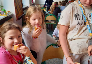 Dwie uczennice z klasy 5a ( bliźniaczki) jedzą kanapeczki z konfiturą wiśniową, uśmiechając się przy tym. Po prawej stronie dwie uczennice smarują kanapki konfiturą.