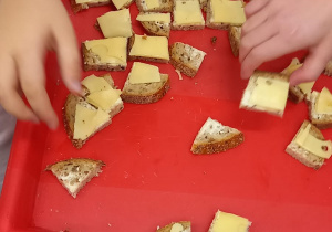 Na czerwonej tacy leżą małe kromki chleba z masłem i żółtym serem.