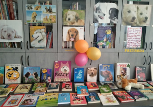 Na stolikach bibliotecznych leżą książki o psach. Na szafach wiszą plakaty z wizerunkami psów i wiersz napisany przez ucznia. Pośrodku Wisza trzy balony.