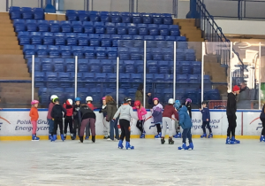 Uczniwie stoją na lodowisku przy bandzie.