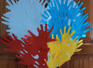 Serce wykonane z wyciętych z papieru dłoni. Po lewej stronie dłonie są biało-czerwone, a po prawej niebiesko-żółte.