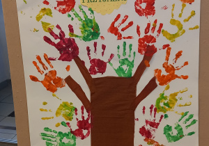 Drzewko Przyjaźni. Pień i gałęzie wykonane z brązowej bibuły. Liście to żółte, czerwone, pomarańczowe i zielone dłonie dzieci odbite w farbie.