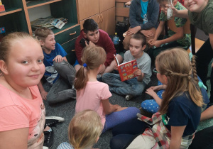 Świetlica szkolna. Dzieci siedzą na dywanie, jeden z chłopców czyta im książkę Grzegorza Kasdepke "Bon czy ton".