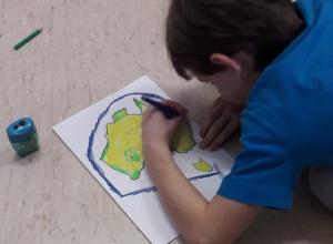 Chłopiec koloruje mapę Australii. Obok leży temperówka i kredka.