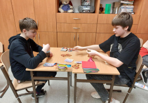 Dwaj chłopcy siedzą przy stoliku i grają w gry.