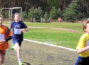 Chłopcy w strojach sportowych biegną po bieżni.