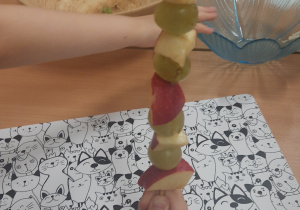 Dziecko trzyma owocowy szaszłyk wykonany z jabłek i winogron.