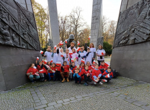 Przy pomniku wychowaczynie oraz dzieci są ubrani w białe i czerwone koszulki. Machają polskimi flagami.
