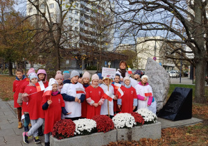 Wychowawczyni wraz z uczniami stoi przy pamiątkowej tablicy na Powiślu. Wszyscy są ubrani w białe lub czerwone koszulki.