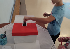 Chłopiec wrzuca do pudełka kartę do głosowania.