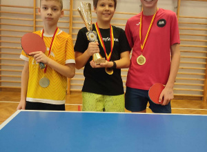 Trzech uczniów szkoły prezentuje medale oraz puchar zdobyte w tenisie stołowym.