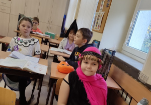 Dzieci i goście z bajek siedzą w klasie przy stolikach.