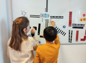 Dziewczynka i chłopiec ustawiają elementy na planszy zgodnie z zasadami ruchu drogowego.