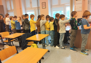 W szkolnej sali uczniowie są ustawieni jeden za drugim w trakcie zajęć warsztatowych.