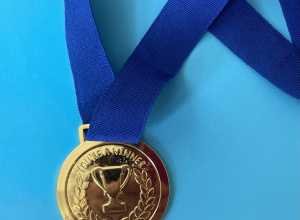 Na niebieskim tle leży medal w złotym kolorze na granatowej tasiemce.