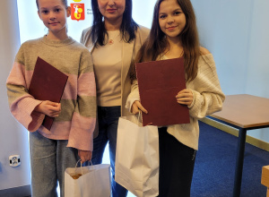 Dwie uczennice stoją w towarzystie Pani Wiceburmistrz, Magdaleny Wojciechowskiej. Obie trzymają w ręku dyplom i torbę z upominkami.