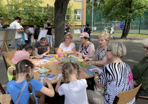 Przy stoliku siedzą panie i uczennice. Dzieci kolorują prace. fot. p. A. Niewczas