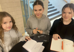 Trzy uczennice prezentują otrzymane autografy - w tym jeden na czepku pływackim.