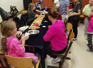 Uczniowie siedzą wokół stolika z wróżbami. Po prawej stronie w różowym swetrze siedzi nauczycielka.