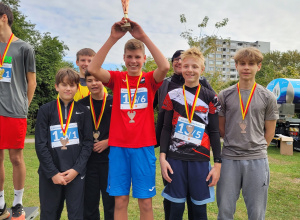 Sześciu uczniów stoi na podium. Stojący pośrodku chłopiec, trzyma wysoko nad głową puchar.