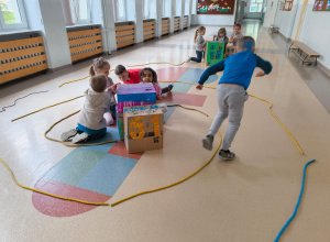 Dzieci są zaangażowane w zabawę kreatywną, wykorzystując do tego pudełka kartonowe ozdobione rysunkami i kolorowym papierem – niektóre z nich przypominają budynki z oknami.