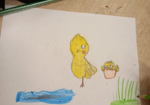 Na zdjęciu można zobaczyć ilustrację, na której są dwa kurczaki. Jeden stoi bokiem na jednej nodze. Drugi jest mniejszy i siedzi w pękniętym jajku. Na ilustracji znajduje się również fragment stawu i zielonej trawy.