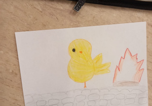 Na zdjęciu znajduje się ilustracja z żółtym kurczakiem, który stoi odwrócony plecami do ogniska.
