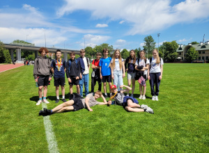 Na zdjęciu widoczna jest grupa trzynastu uczniów - dziewięciu chłopców i cztery dziewczynki - stojących na zielonej murawie stadionu lekkoatletycznego w słoneczny dzień.