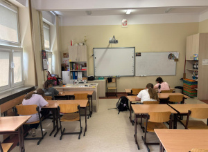 Na zdjęciu widać klasę szkolną, w której kilka uczennic siedzi przy ławkach i pisze.