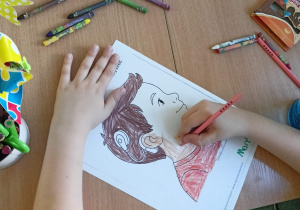 Uczeń koloruje rysunek dziecka z aparatem słuchowym. Na stoliku leżą kolorowe kredki i plastelina.