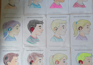 Na stoliku leży dwanaście kolorowanek przedstawiających dziewczynki i chłopców z aparatami słuchowymi lub implantami ślimakowymi. Rysunki są pokolorowane według preferencji uczniów.